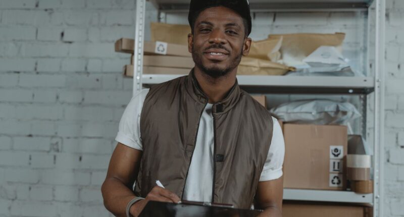Warehouse employee holding a clipboard surrounded by packages, representing a weekly operations review