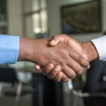 Two people shaking hands over a deal, representing the choice between equity and salary