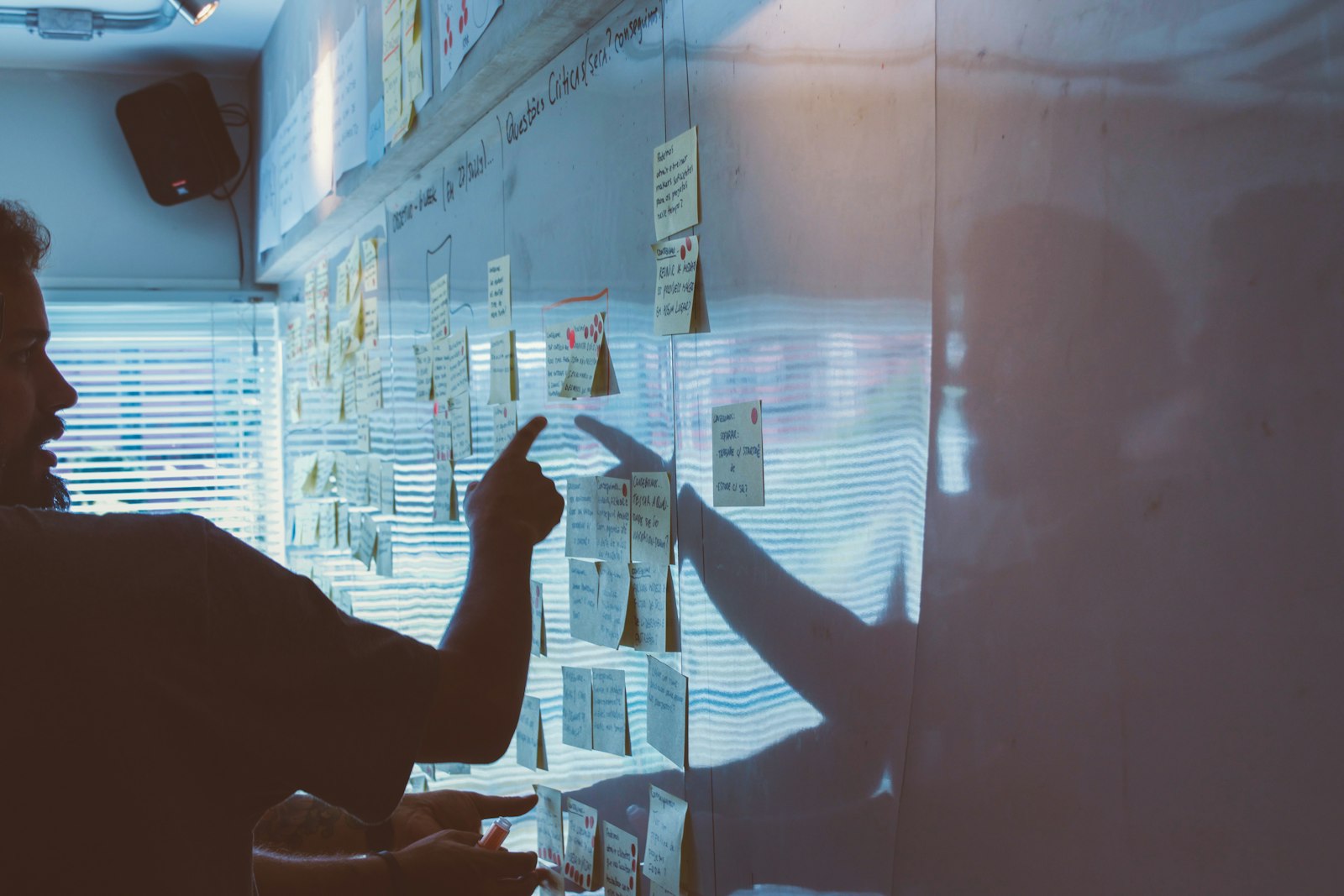 Person pointing at notes on a wall, representing researching and analyzing competitors
